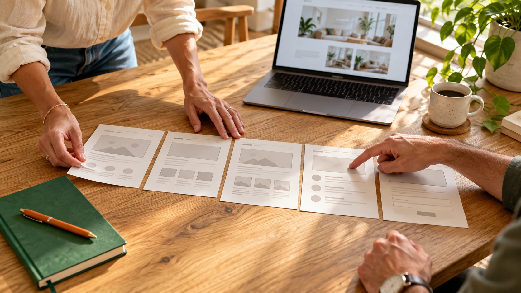 Two professionals arranging website page plans beside a laptop in a sunlit workspace